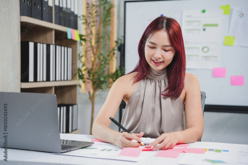 Asian businesswoman is smiling while writing on sticky notes during a productive day at the office Asian businesswoman is smiling while writing on sticky notes during a productive day at the office