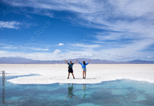 Young man and woman in love posing in the Salinas Grandes of Argentina during their vacation at the edge of a blue lake in which they are reflected. photo