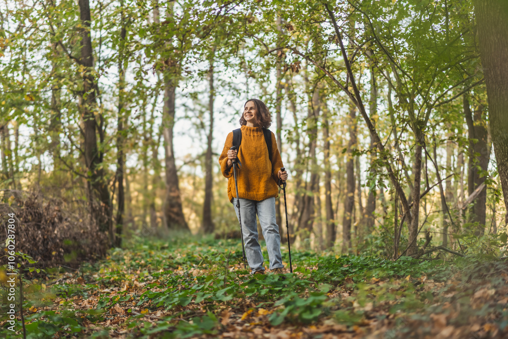 Woman with backpack and trekking poles hiking over the autumn forest