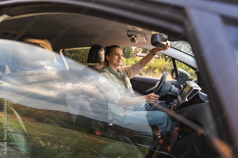 Young female driver adjusting rear view mirror while sitting in car