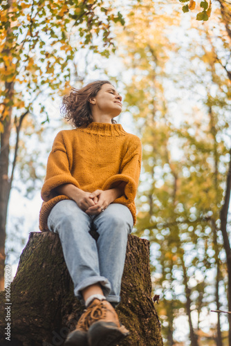 Obraz na płótnie Young Caucasian woman enjoying autumn nature and weather sitting on a tree stump in autumn forest w salonie