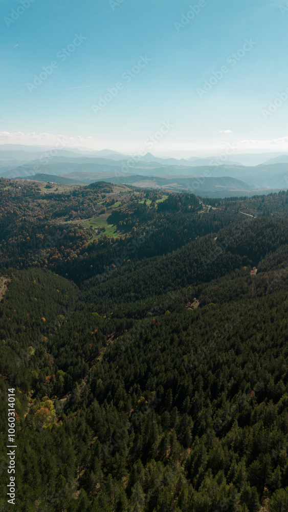Obraz premium Beautiful view of green fields, small villages and mountain peaks. Multicolored green and yellow mixed forest of western Serbia in early autumn. Aerial view from a drone. Tornik Mountain.