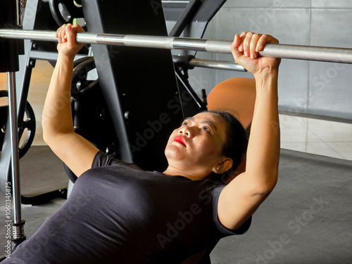 40 year old Asian woman doing weight training to build muscle mass, doing bench press exercises in the gym