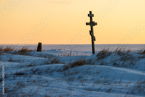 Orthodox cross in the snowy tundra on the coast of the frozen sea. An old cemetery in the far North of Russia in the Arctic. Snow-covered grave. Cold winter weather. Chukotka, Polar Siberia, Russia.