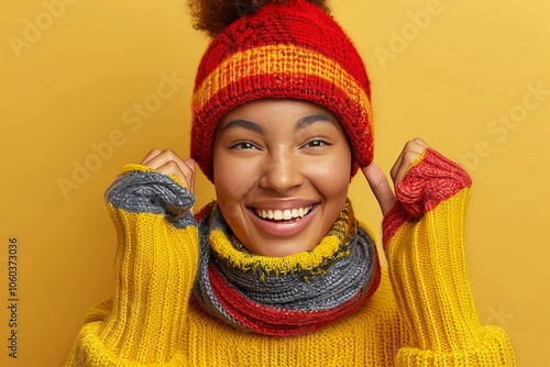 Smiling young woman wearing a colorful winter sweater and hat against a vibrant yellow background during a chilly day