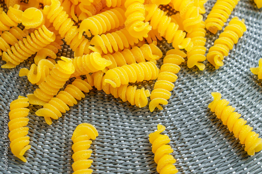 Spiral fusilli pasta spread on a textured mat. Raw ingredients for traditional Italian cuisine. Organic food themes Spiral fusilli pasta spread on a textured mat. Raw ingredients for traditional Italian cuisine. Organic food themes