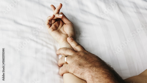 Obraz na plátně A close-up of a couple's hands intertwined on the bed, capturing a moment of relaxation and intimacy