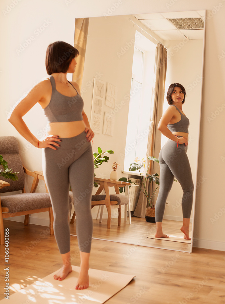 Obraz premium Sporty young woman in sportswear doing stretching exercises at home.