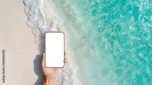 Obraz na płótnie A person holds a smartphone above clear turquoise water and sandy beach, showcasing a relaxing summer vibe. w salonie
