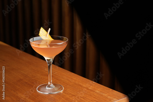 Bronx cocktail glass with orange peel slice on a wooden bar counter, background with copy space