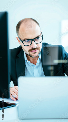man a suit glasses focuses on his laptop