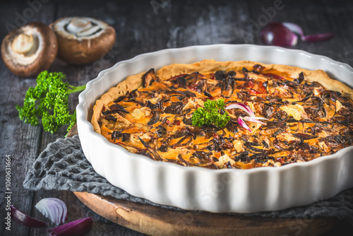 Tart, quiche, with caramelized mushrooms, red onions and parsley on a dark background