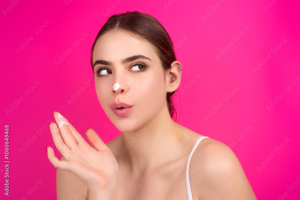 Fototapeta premium Beauty portrait of a beautiful half naked woman applying face cream isolated on studio background. Skin care product. Moisturizing creme on face. Perfect skin, morning routine.