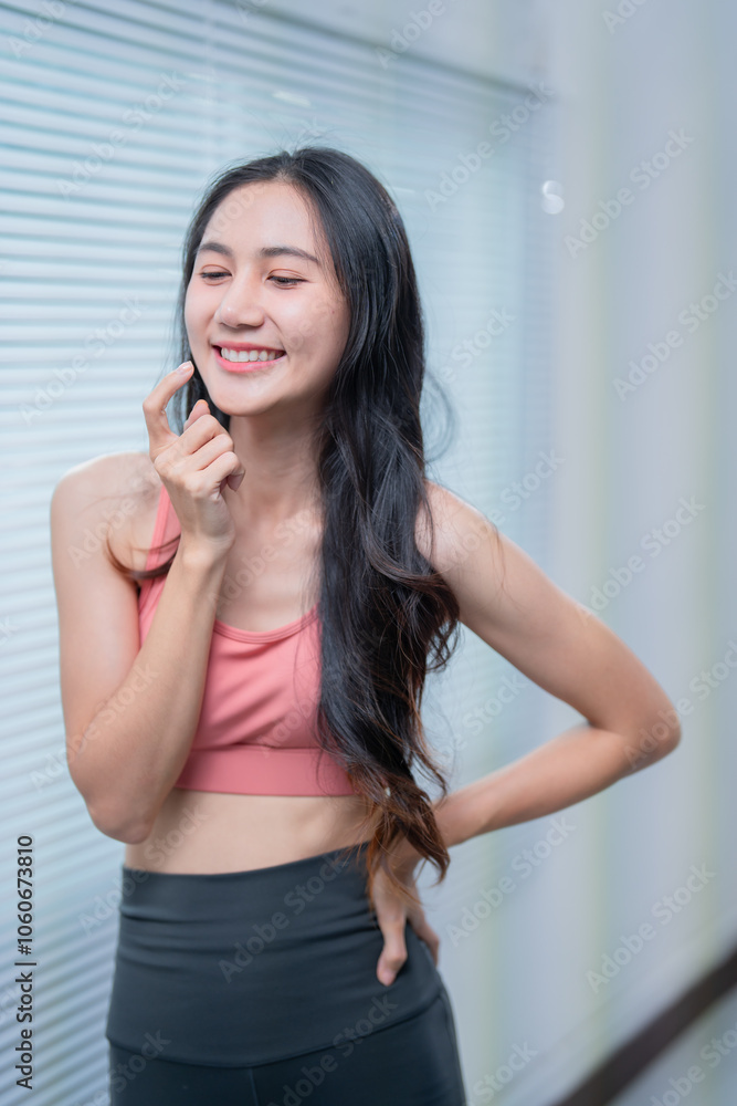Smiling asian fitness woman is applying cream on her face after a workout session at home, promoting skincare and wellness Smiling asian fitness woman is applying cream on her face after a workout session at home, promoting skincare and wellness