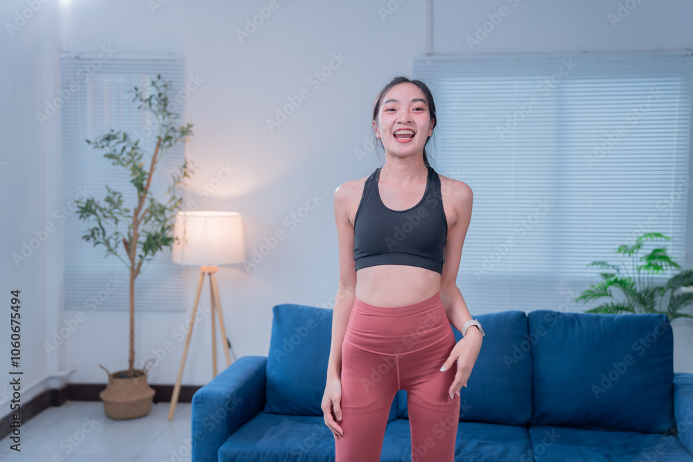 Asian woman in sportswear exercises happily at home, surrounded by furniture and plants, basking in natural light. Her smile shows dedication to wellness Asian woman in sportswear exercises happily at home, surrounded by furniture and plants, basking in natural light. Her smile shows dedication to wellness
