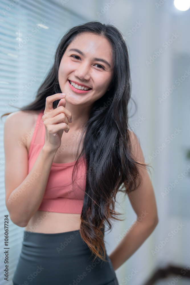 Active asian woman smiles while applying face cream before her workout routine at home, showing her dedication to health and beauty Active asian woman smiles while applying face cream before her workout routine at home, showing her dedication to health and beauty