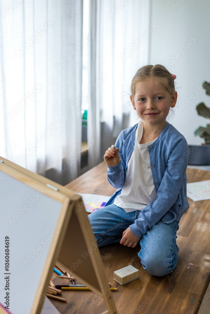 A determined 5-year-old girl focuses on writing letters with chalk on a board, engaging in her studies. A determined 5-year-old girl focuses on writing letters with chalk on a board, engaging in her studies.