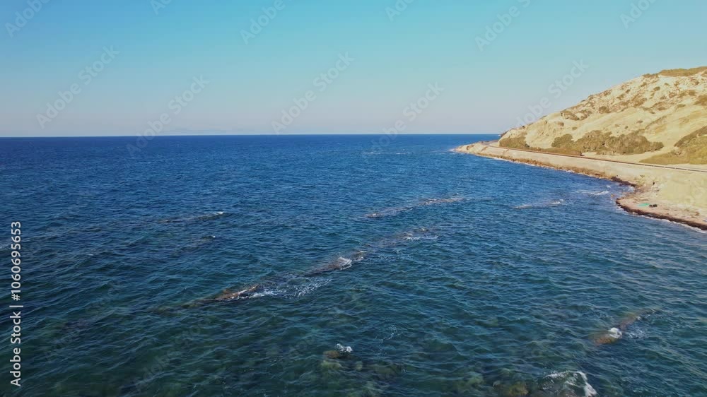 Calm ocean waves near rocky coastline during clear blue sky Calm ocean waves near rocky coastline during clear blue sky