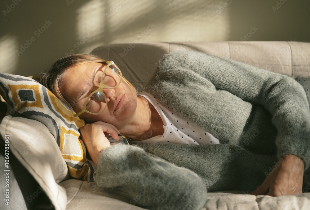 Mature woman is lying on couch at home closed eyes. Middle aged woman is tired and exhausted. Health problems, suffers migraine, high blood pressure, aging process or menopause concept. Mature woman is lying on couch at home closed eyes. Middle aged woman is tired and exhausted. Health problems, suffers migraine, high blood pressure, aging process or menopause concept.