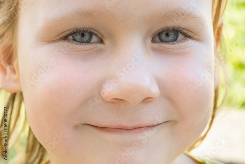 Close up of face of child girl looking at camera with happy smile on summer sunny day