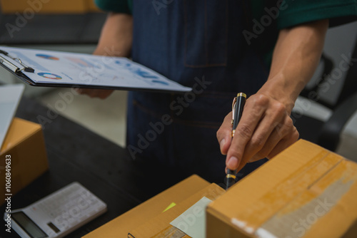 An Asian man carefully prepares a package for a customer's online order, methodically placing items in a box, sealing it securely, and attaching a shipping label for prompt delivery.