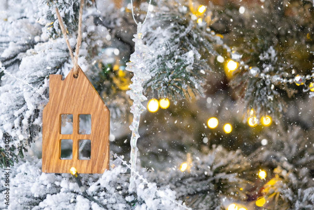 Naklejka premium Key and tiny house keychain in hand on background fairy lights Christmas tree. gift for New Year, Christmas. Building, design, project, moving, insurance, mortgage, rent and purchase real estate.
