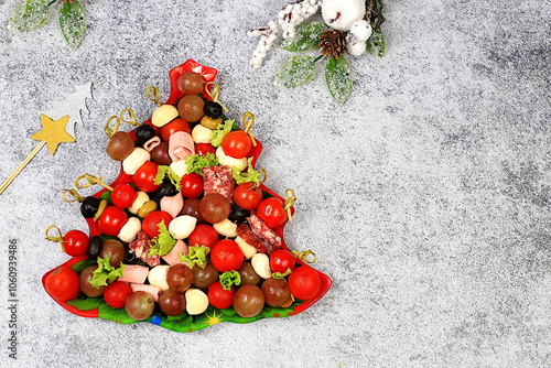 Christmas and New Year's dishes, a set of snacks for the festive table. Plate with Christmas tree of tomatoes, pate, mozzarella cheese, salami, olives, black olives and grapes on a concrete table,