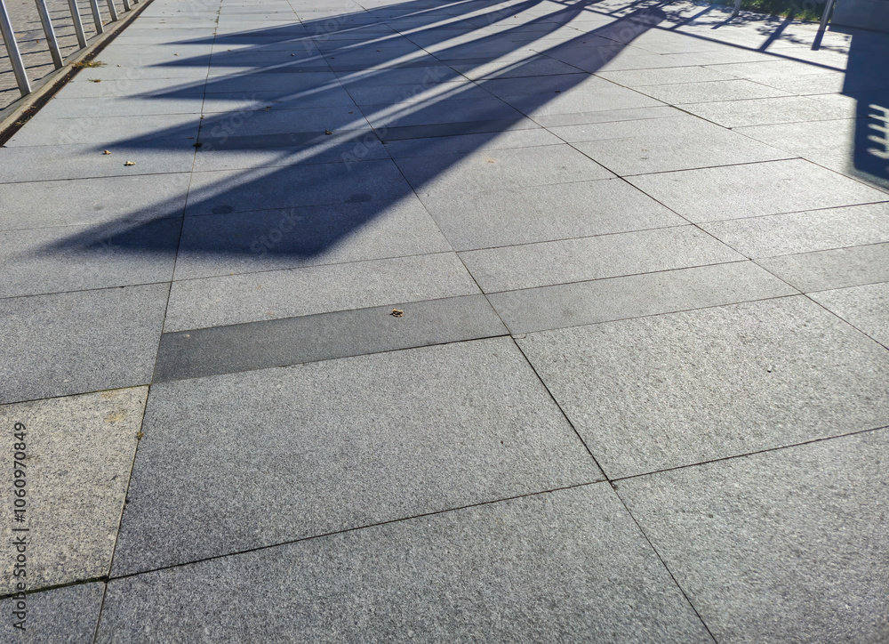 Fototapeta premium Sunlit pavement showing shadows, creating an abstract pattern. Ideal for backgrounds or architectural projects.
