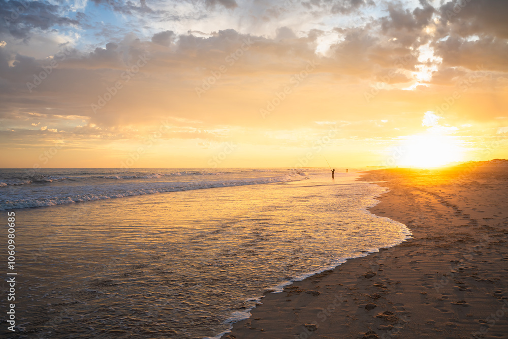 Footprints lead along the shoreline bathed in early morning light.