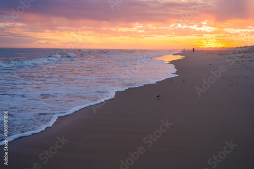 Intense sunset colors of red, purple, and orange fill the sky and reflect on the shoreline.