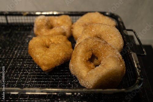 Golden doughnuts sprinkled with sugar cooling on a wire rack. These freshly fried doughnuts are soft on the inside and crisp on the outside, perfect for festive or holiday gatherings. photo