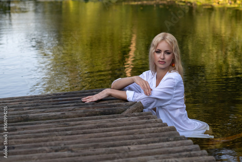 Portrait of a young beautiful blonde girl in a white shirt near the river.