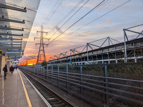 London - 03.14.2024: Passengers waiting for a train at the Custom House Elizabeth Line station behind the yellow line next to the Excel Exhibition Centre during sunrise with the sun at the horizon