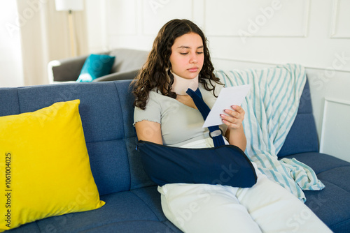 Fotografie Hispanic teenager recovering from accident, sitting on sofa with neck brace and