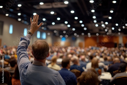 Middle-aged person from behind raising hand to ask question in large seminar, focused lighting on gesture, indoor, medium close-up on action 2