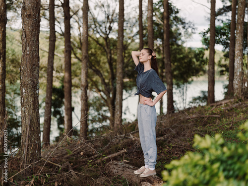 Confident young woman standing in a serene forest, enjoying nature She wears comfortable clothes, exuding a sense of peace and connection with the environment