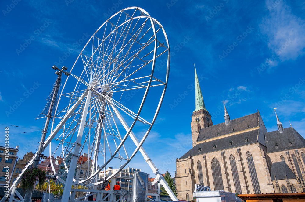 A stunning view of the Ferris wheel in the square in front of St. Bartholomew's Cathedral in Pilsen, adorned with festive lights during the Christmas markets.