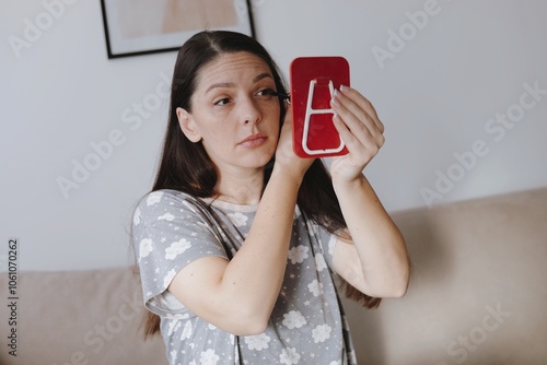 Woman applying mascara while looking at reflection of her mirror.  Morning routine woman wearing pajamas applying her skincare treatments looking at mirror.