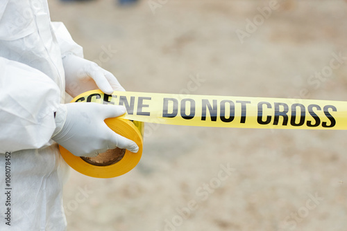 Side view closeup of unrecognizable man wearing protective suit unrolling warning tape with Do not cross sign outdoors and fencing off dangerous site, copy space photo