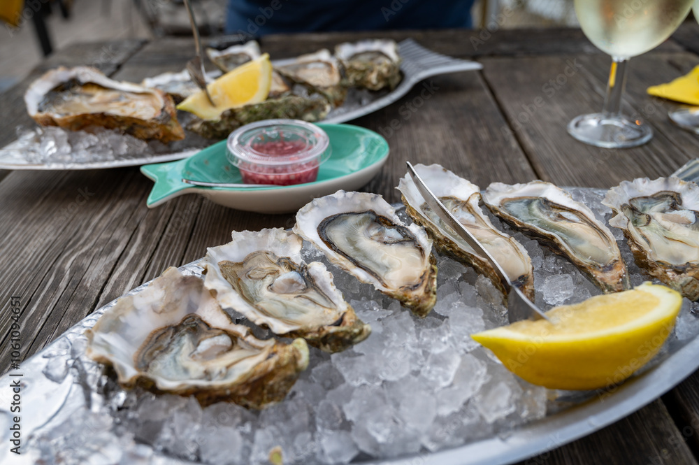 Eating of fresh live oysters with citron at farm cafe in oyster-farming village, Arcachon bay, Gujan-Mestras port, Bordeaux, France in sunny day, huge oyster Eating of fresh live oysters with citron at farm cafe in oyster-farming village, Arcachon bay, Gujan-Mestras port, Bordeaux, France in sunny day, huge oyster