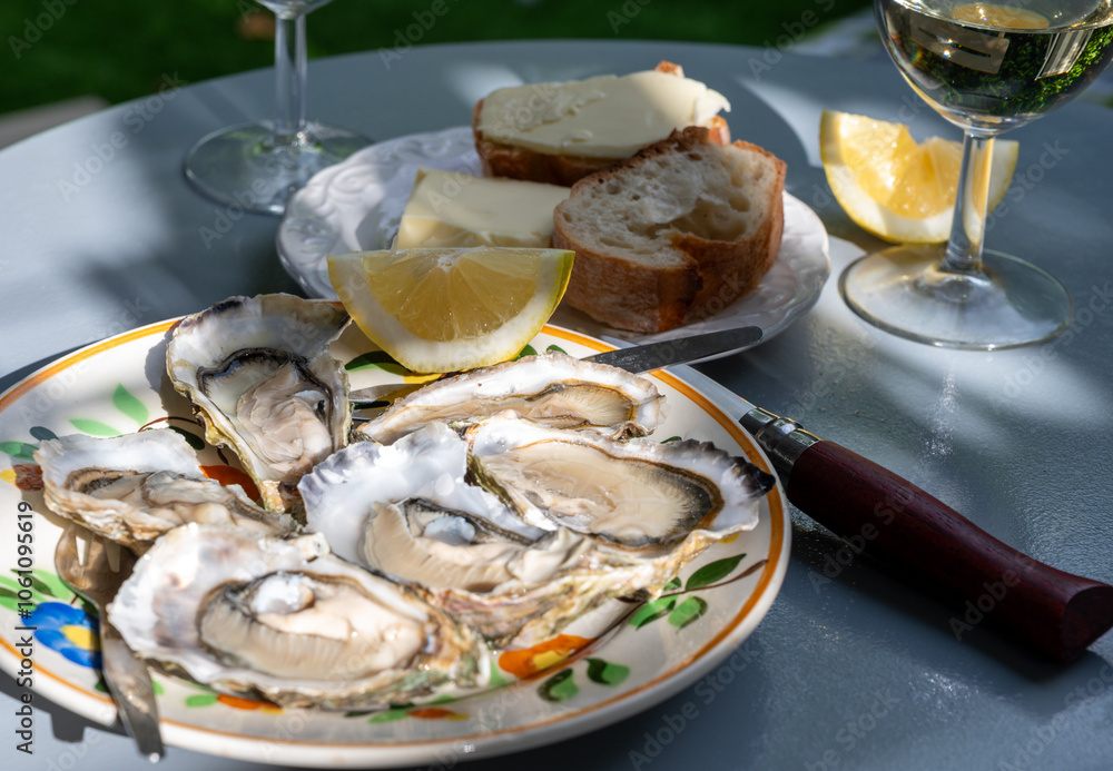 Plate with fresh live oysters with citron, bread, butter and white wine served at restaurant in oyster-farming village, Arcachon bay, Gujan-Mestras port, France Plate with fresh live oysters with citron, bread, butter and white wine served at restaurant in oyster-farming village, Arcachon bay, Gujan-Mestras port, France