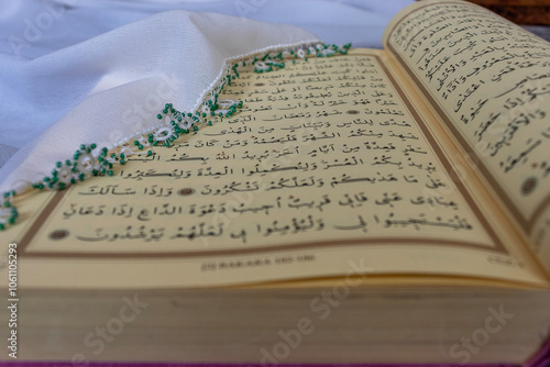 Photo of an open page from the Holy Quran. A verse from the Surah Al-Baqara regarding the month of Ramadan is also visible in the photo. The verse reads, "We sent down this Quran in the month of Ramad