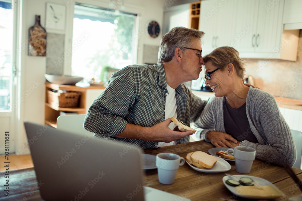 Happy senior mature couple laughing while eating at kitchen table Happy senior mature couple laughing while eating at kitchen table
