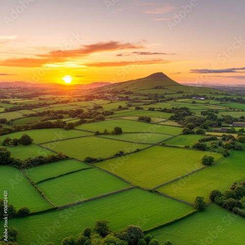 Sunset over a rolling green landscape with a hill in the distance.