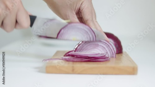 A close up shot of hands cutting red onion to slices on a wooden board, shiny silver knife. Slicing red onion, Cutting red onion , Chopping vegetables on wooden cutting board.