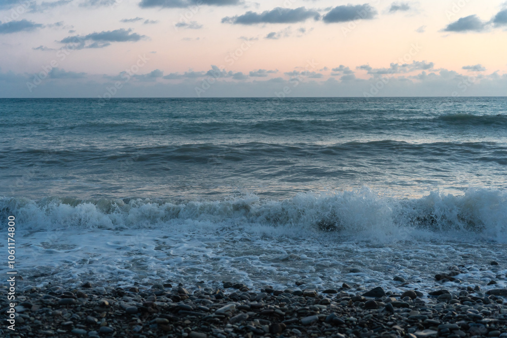 Sea waves roll onto the pebbly shore against the background of the evening sunset sky with clouds. Sea waves roll onto the pebbly shore against the background of the evening sunset sky with clouds.