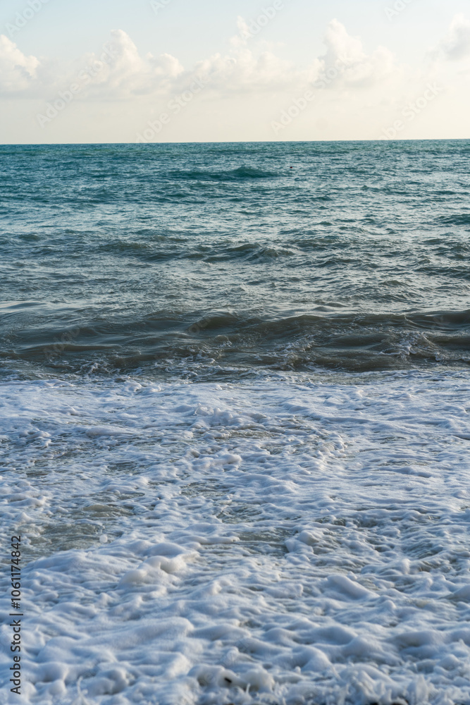 The sea waves roll onto a pebble sea shore against a blue sky with clouds. The sea waves roll onto a pebble sea shore against a blue sky with clouds.