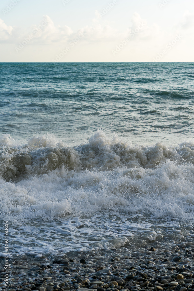 The sea waves roll onto a pebble sea shore against a blue sky with clouds. The sea waves roll onto a pebble sea shore against a blue sky with clouds.