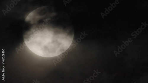 4k video of high thin clouds sailing across the face of a large full moon as it drifts lower in the dark night sky on October 17, 2024.