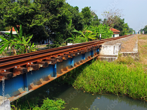 A small railway bridge crosses a small river on a sunny day.